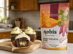 Chocolate cupcakes with pistachio buttercream, one halved to show the pistachio cream center, beside a Nobis Sweet Potato Flour pouch.