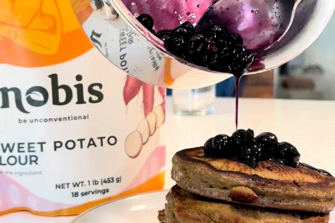 Blueberry lemon maple sauce poured over a stack of nobis sweet potato flour pancakes